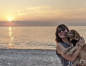 Megan holds her small dog in front of a sunset on Lake Erie